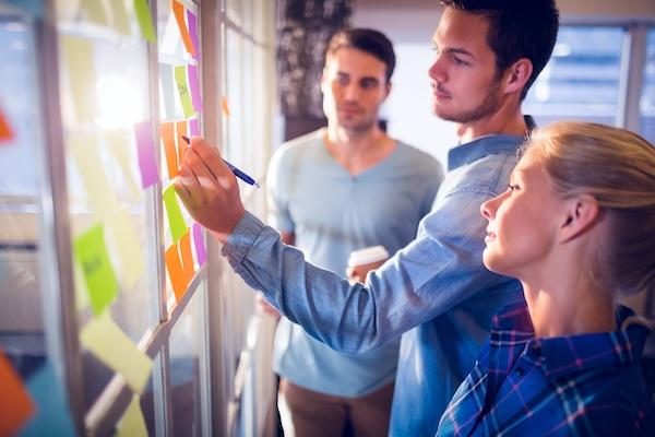 two men and a woman looking at sticky notes on glass