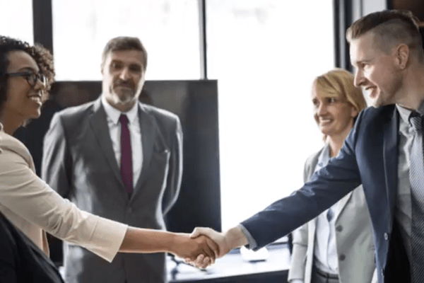 man and woman shake hand with other professionals behind them