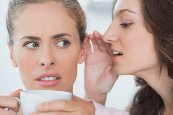 Women whispering a secret into another women's ear