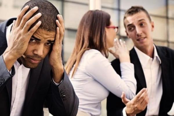 man with head in hands while another man and woman seem to be gossiping