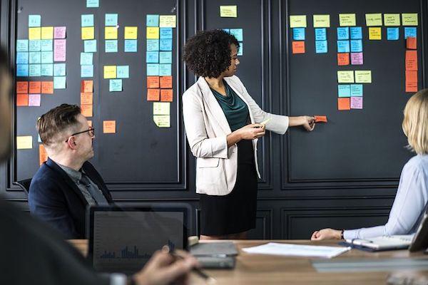 black woman standing in front of coworkers with sticky notes all over the board behind her