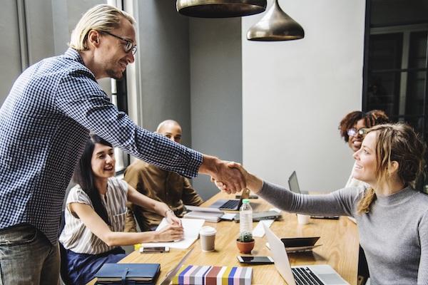 coworkers at a conference table and man and woman shaking hands