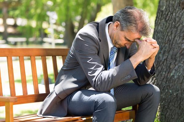 older man in business suit on a bench with head in hands looking defeated