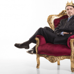 business man with crown sitting across a throne-like chair