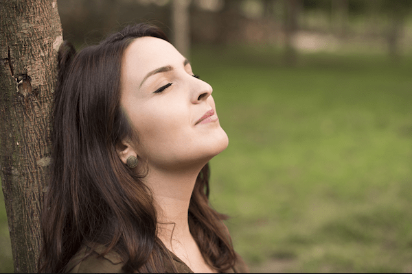 woman leaning against a tree with her eyes closed