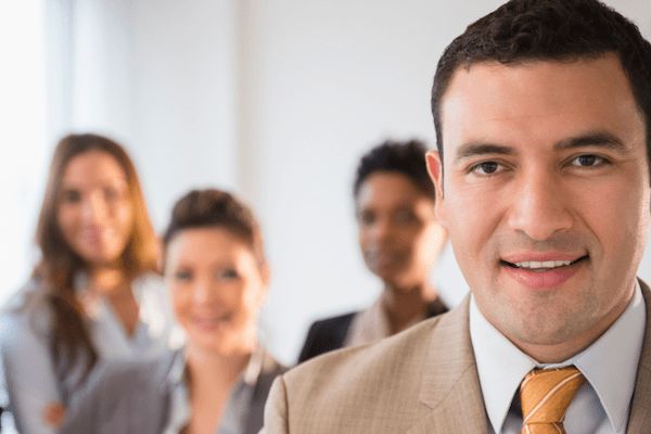 Hispanic man in suit smiling in forefront with people blurred in the background