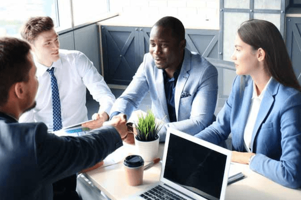 business people around table with two men shaking hands