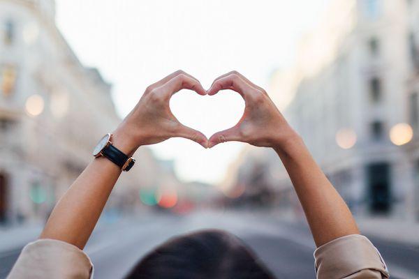 hands making a heart shape in front of a street blurred in the background