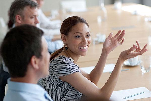 Women speaking at a table of colleagues in a meeting room