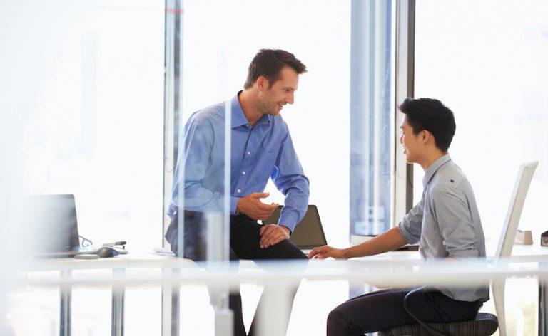 professional man sitting on table talking with younger man in chair