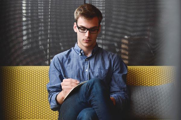 man sitting on couch writing in book or notepad