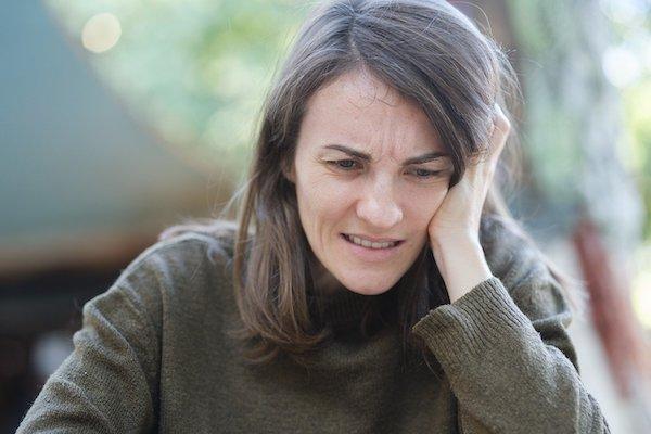 woman with grimace and hand on head looking stressed