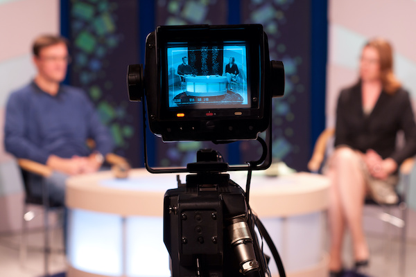 video camera in front of man and woman talking in a studio