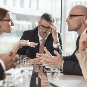 professionals arguing across conference table with man at the head of it looking defeated and discouraged