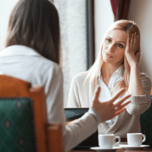 two woman at a cafe looking frustrated with each other