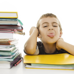 boy student sticking out tongue by stack of books